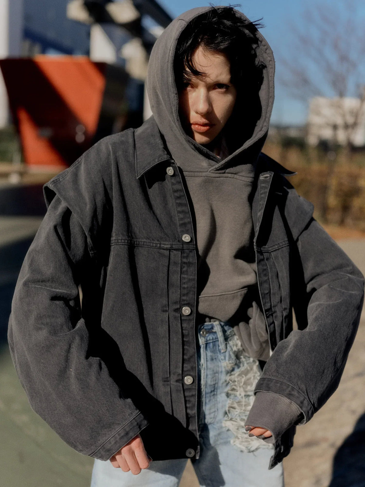 Model wearing a black denim jacket over a hooded sweatshirt with distressed denim